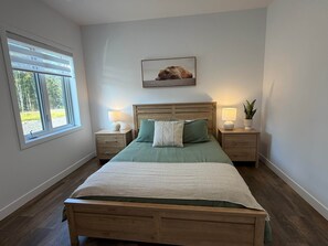 Quarto com cama de madeira, duas mesas de cabeceira com abajures, janela com persianas e um quadro na parede.