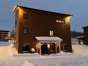 A two-story building with a snow-covered entrance and illuminated string lights.