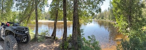 Joki, jonka ympärillä on tiheää metsää, ja joen vasemmalla puolella on pysäköitynä mönkijä.