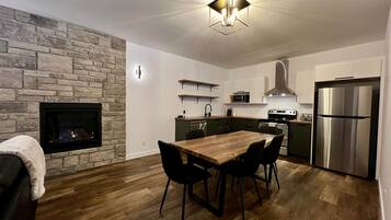 Une cuisine moderne avec un mur en pierre, un plancher en bois, une table à manger avec des chaises, une cuisinière encastrée et un réfrigérateur en acier inoxydable.