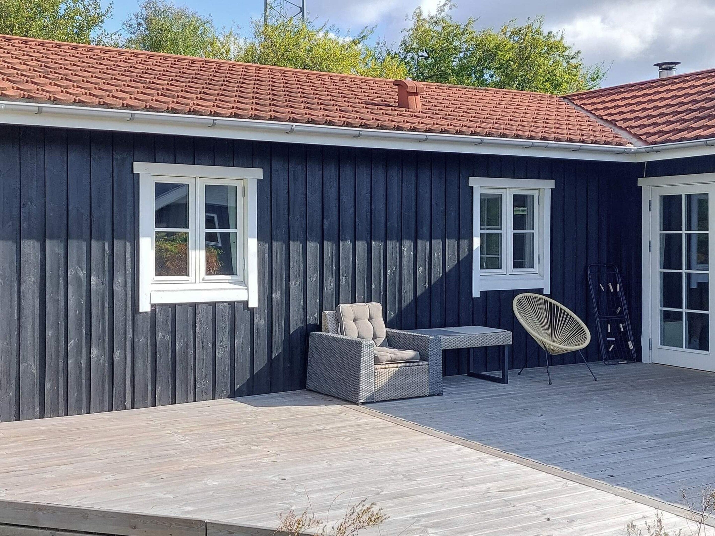 A dark wooden building with two windows and a covered patio area with outdoor furniture.