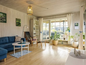 Ein Wohnzimmer mit einem blauen Sofa, einem runden Couchtisch, einem Bücherregal und einem großen Fenster mit Vorhängen.