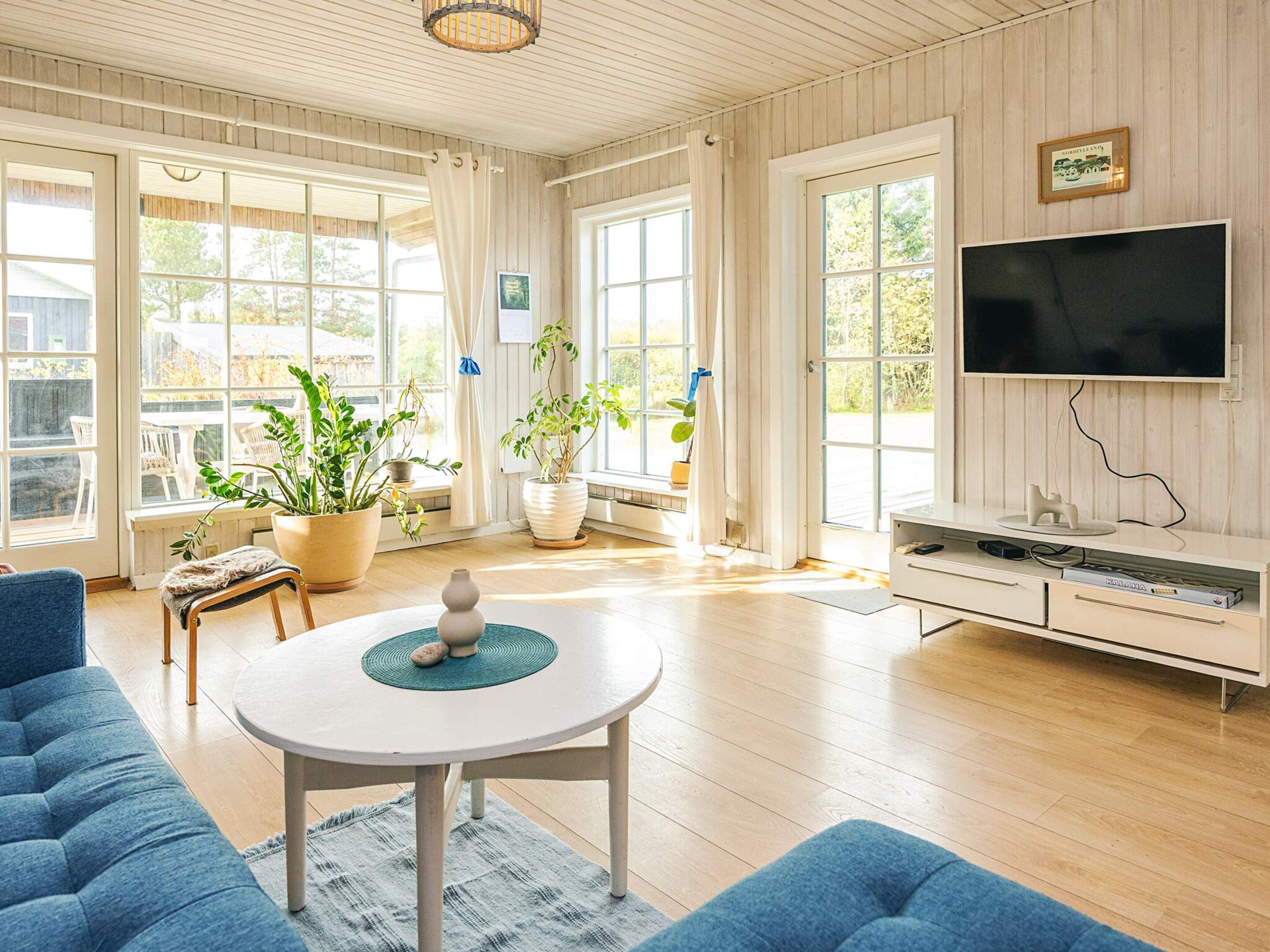 A spacious living room with a large TV, comfortable seating, and potted plants.