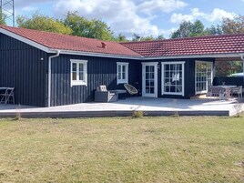 Un edificio de dos pisos con techo de tejas rojas, ventanas amplias y un patio cubierto con mobiliario exterior.