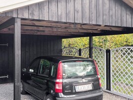 Un coche negro estacionado bajo un porche de madera con un cerramiento de celosía al fondo.