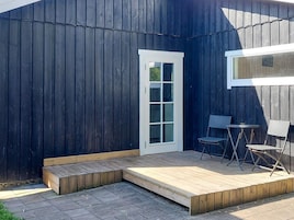 Una terraza de madera con una puerta blanca, una mesita y dos sillas.