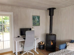 Quarto com escrivaninha, cadeira, cama, lareira a lenha preta e janela com vista para o verde.