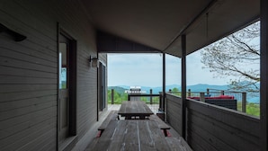 Eine überdachte Veranda mit einer Holzbank und einem Grill, mit Blick auf eine reizvolle Landschaft mit Bergen und einem Gewässer.