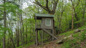 Ein Baumhaus mit einer Holztreppe und einem Fenster, umgeben von einem Wald.