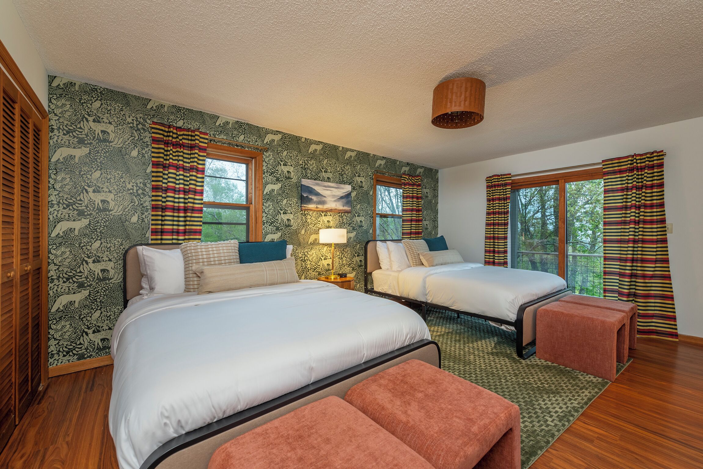 A bedroom with two beds, a nightstand, a lamp, and a view of the outdoors.