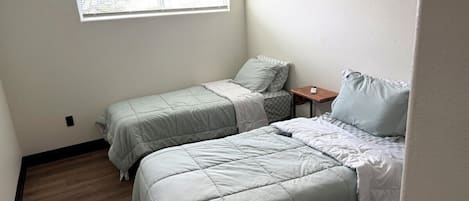 A bedroom with two beds, a small table, and a window.