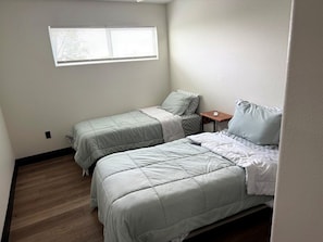Une chambre avec deux lits, une petite table et une fenêtre.