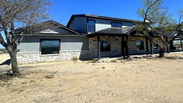 Una casa de dos pisos con fachada de piedra, ventanas amplias y un porche cubierto.