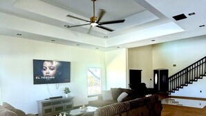 Amplia sala de estar con ventilador de techo, televisor y escalera que sube a un nivel superior.