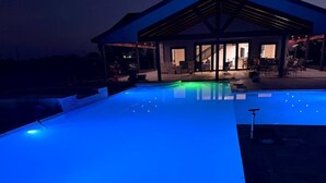 Una piscina con iluminación azul, un patio cubierto y un edificio con entrada abierta.