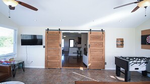 A spacious living area with a sliding barn door, a foosball table, a television, and a dining area in the background.