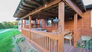 Una terraza de madera con mobiliario exterior, una lámpara colgante y vistas del paisaje circundante.
