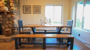 Un comedor con pared de piedra, una mesa de madera, bancos y una ventana con vistas.