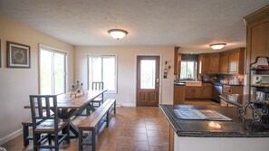 Una cocina amplia con armarios de madera, un comedor con una mesa larga y bancos, y un gran ventanal que proporciona luz natural.