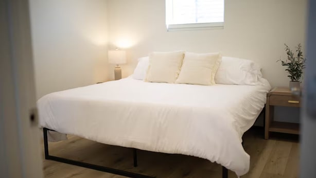 Une chambre à coucher avec un lit, une table de chevet, une lampe et une fenêtre.