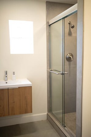 A modern bathroom with a glass shower enclosure, a wooden cabinet, and a white countertop. - 3-bedroom house in nice Clovis with cool AC for relaxing stays (Clovis)