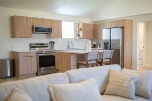 A modern kitchen with wooden cabinets, stainless steel appliances, and a central island with chairs. - 3-bedroom house in nice Clovis with cool AC for relaxing stays (Clovis)