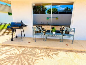 An outdoor patio with a grill, metal chairs, and a table with a potted plant.