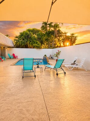 An outdoor pool area with lounge chairs and a sunset view.