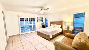 A bedroom with a bed, a nightstand, a chair, a ceiling fan, and a window with blinds.