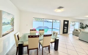 Zona pranzo con tavolo e sedie in vetro, divano e vista su una piscina.