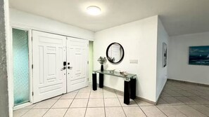 A hallway with a double door, a glass console table, a mirror, and a framed picture on the wall.