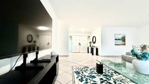 A modern living room with a flat-screen TV, a glass coffee table, and a patterned rug.