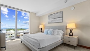 Um quarto espaçoso com uma cama grande, duas mesas de cabeceira, um criado-mudo, uma janela com vista para a cidade e um detector de fumaça no teto.