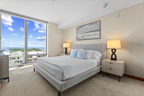 Een ruime slaapkamer met een groot bed, twee nachtkastjes, een venster met uitzicht op de stad en een rookmelder aan het plafond.