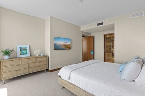 A bedroom with a bed, a dresser, a framed picture, and a door leading to a bathroom. - Ocean View 2BR/2BA at ONE Ala Moana — With 2 Parking Stalls & Resort Amenities (Honolulu)
