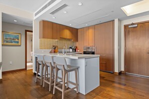A modern kitchen with wooden cabinets, a central island with bar stools, and built-in appliances. - Ocean View 2BR/2BA at ONE Ala Moana — With 2 Parking Stalls & Resort Amenities (Honolulu)