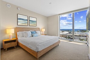 Habitación de hotel con una cama grande, dos lámparas de noche, vista de la ciudad a través de un ventanal amplio y dos cuadros en la pared.