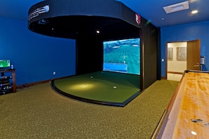 A room with a golf simulation setup, including a screen displaying a golf course and a golf ball on a mat. - Ocean View 2BR/2BA at ONE Ala Moana — With 2 Parking Stalls & Resort Amenities (Honolulu)