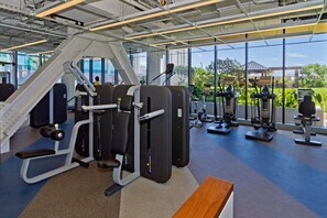 Un gimnasio con diferentes equipos de ejercicio, amplias ventanas y vistas al exterior.