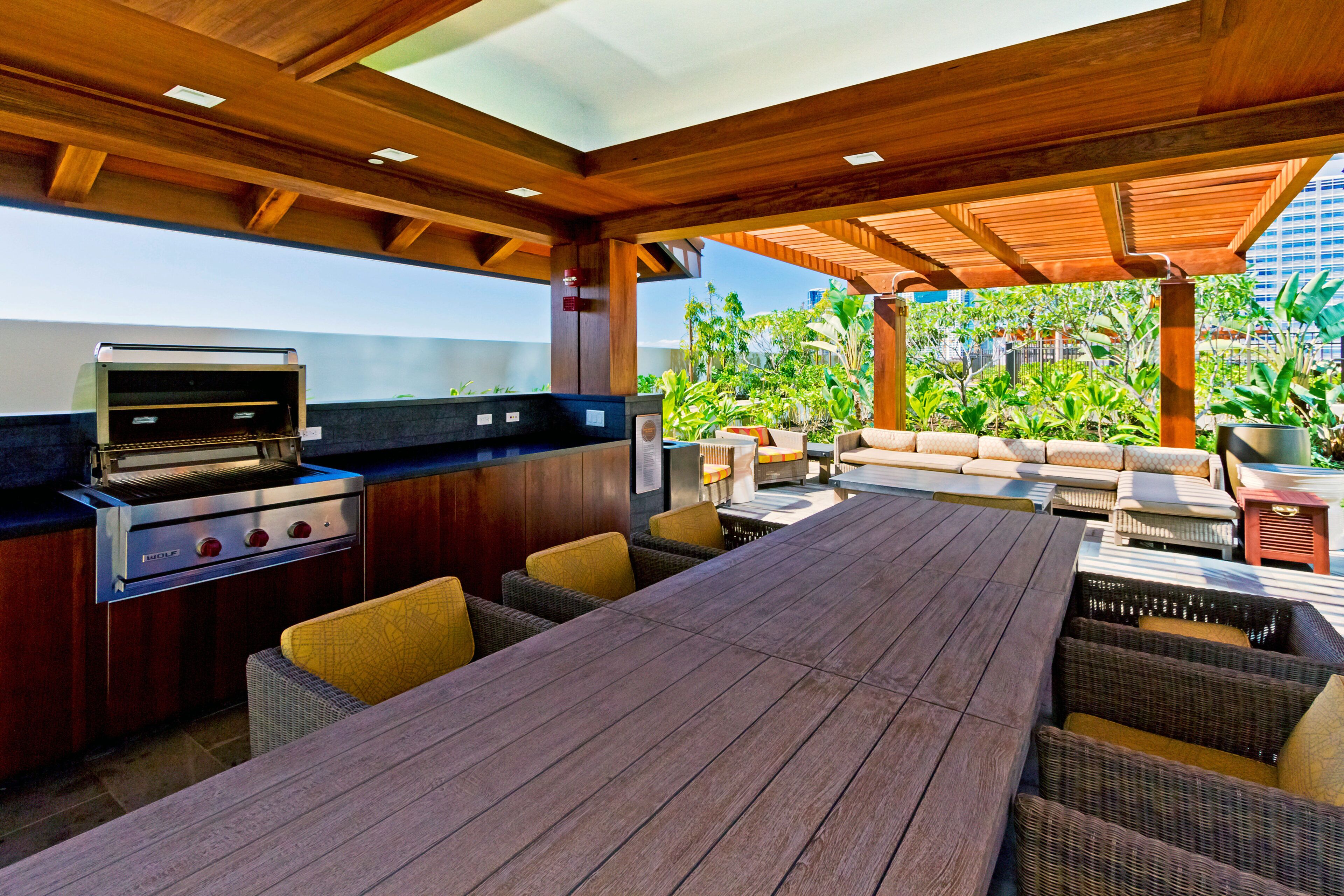 An outdoor patio with a grill, seating area, and a view of greenery.