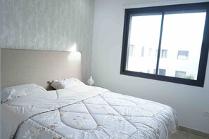 A bedroom with a bed, a nightstand, and a window.