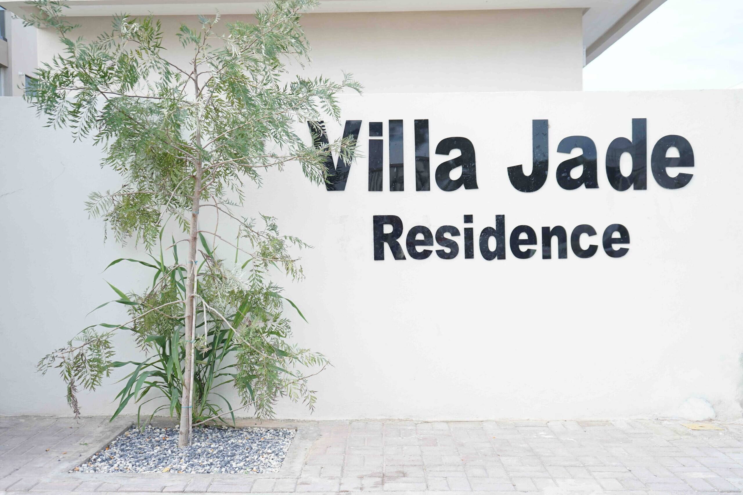Schild für Villa Jade Residence mit einem Baum im Vordergrund.