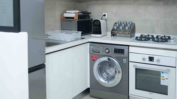 A modern kitchen with white cabinetry, a built-in microwave, a gas stove, a washing machine, and a sink.