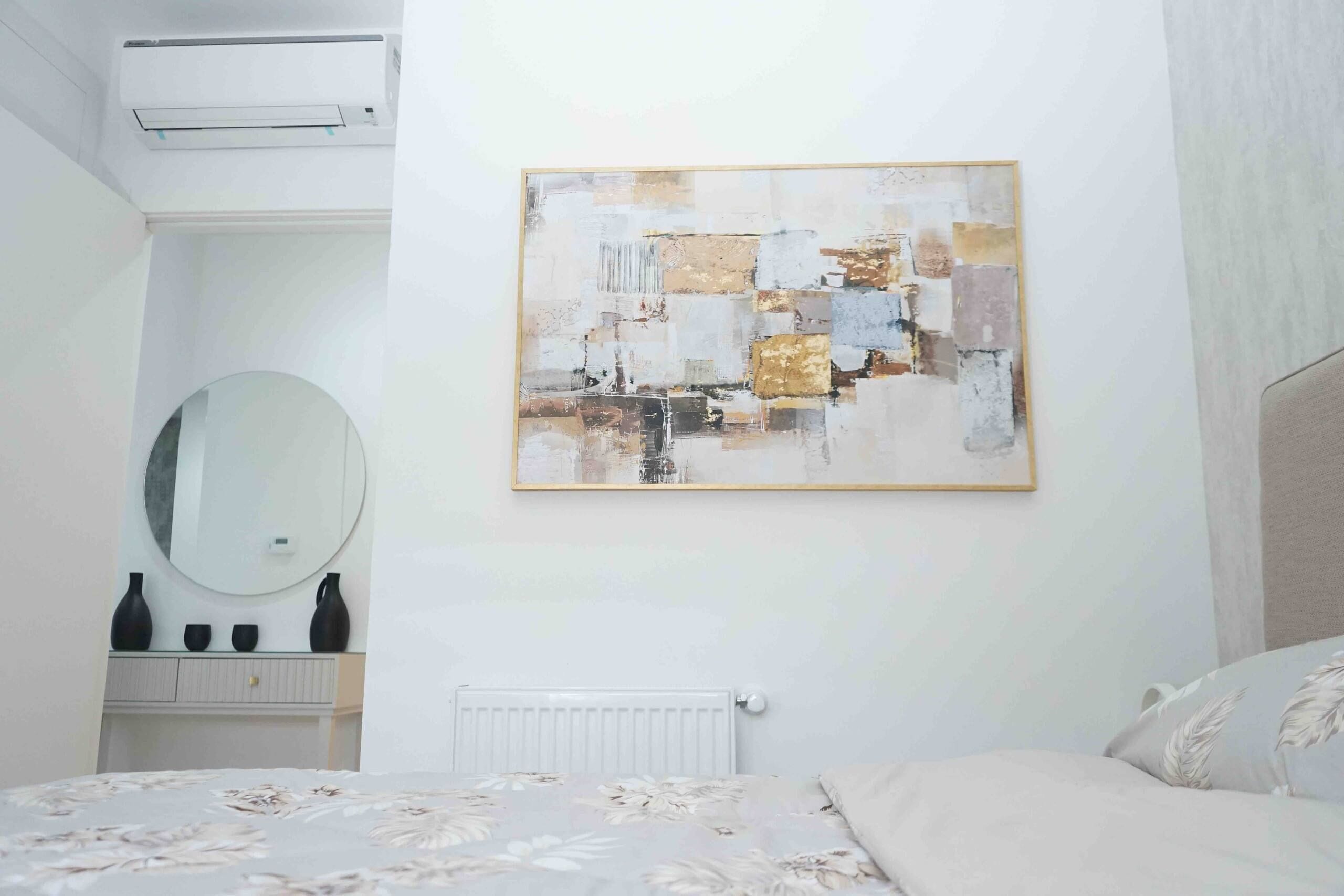A bedroom with a bed, a round mirror, a radiator, and a wall-mounted abstract painting.