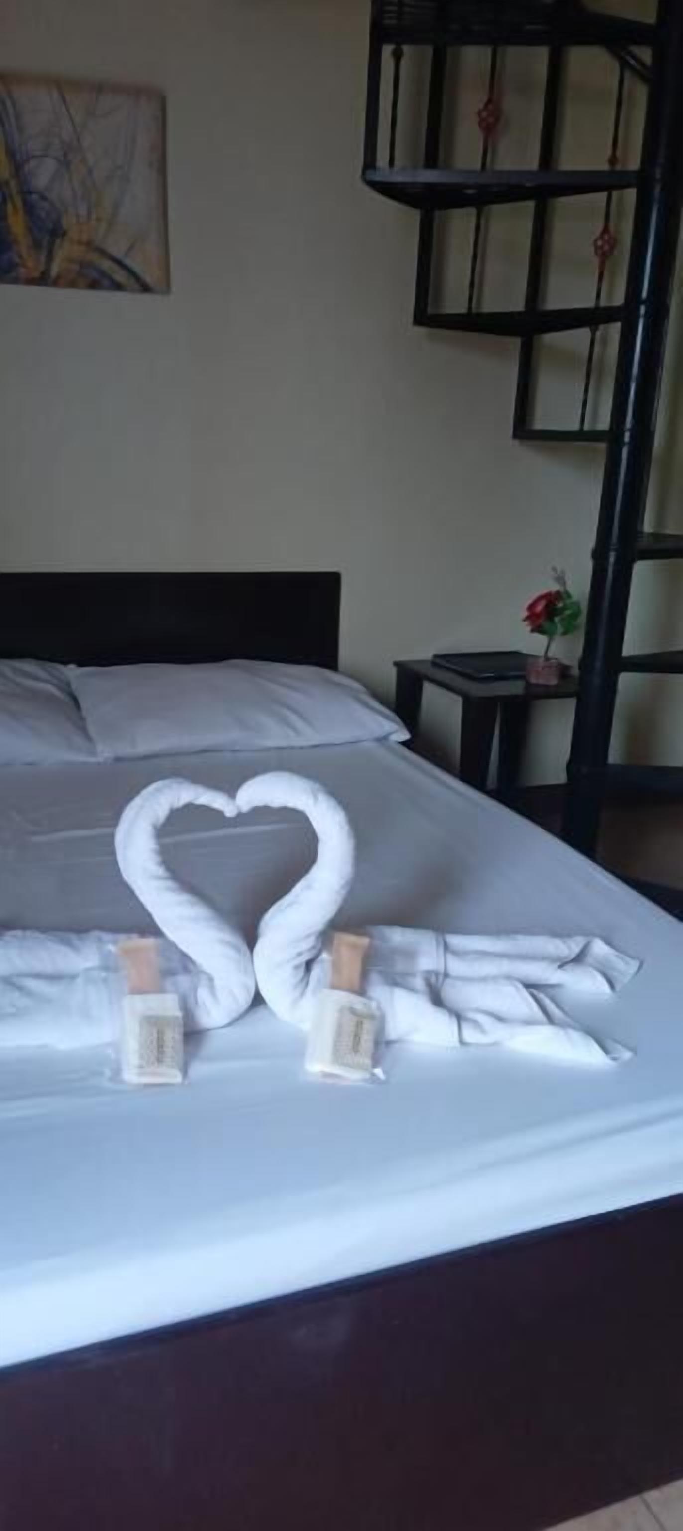 A bed with a heart-shaped towel arrangement and two bottles of lotion.