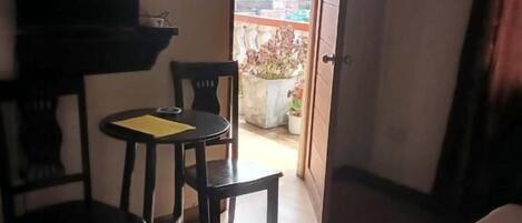 A hotel room with a bed, a small table with chairs, a television, and a view of the outside.