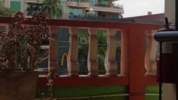 Un balcón con vista a un edificio de varios pisos con el logotipo de McDonald's, una planta en maceta y una barandilla.