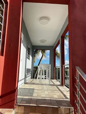 Un couloir au sol carrelé mène à un espace détente d’où l’on peut admirer des palmiers.