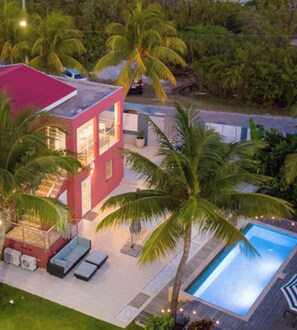 Una casa moderna con piscina, rodeada de palmeras y un césped cuidado.