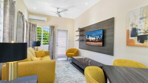 Ein modernes Wohnzimmer mit einer Couch, Sesseln, einem Couchtisch, einem an der Wand befestigten Fernseher und einem Deckenventilator.